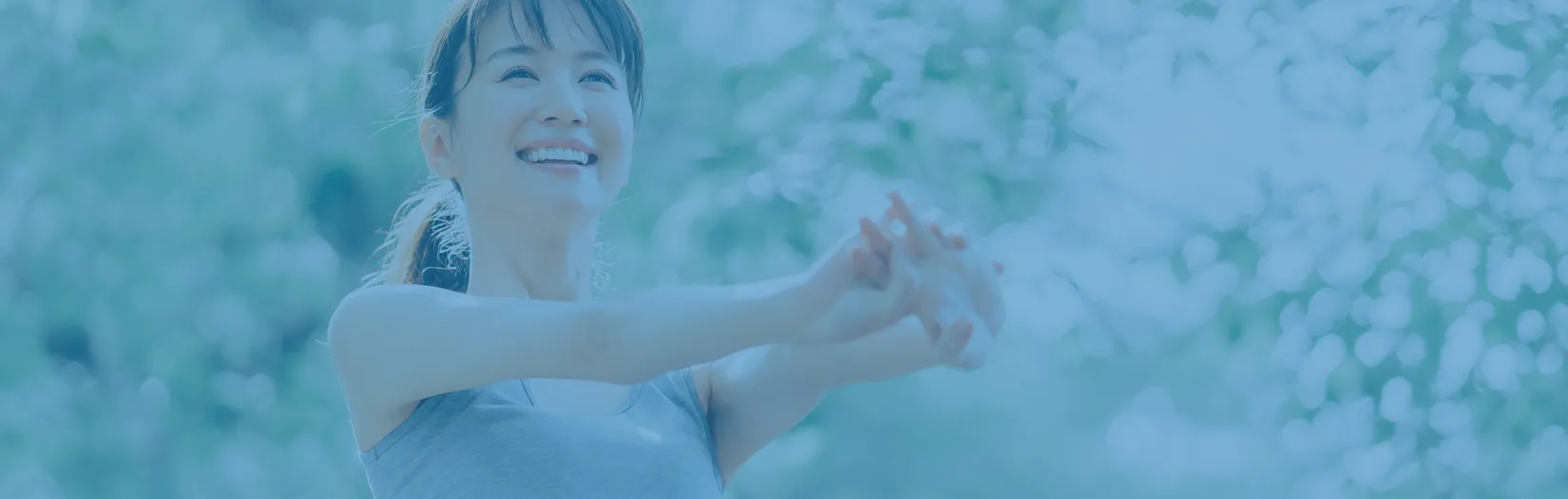 自然光の中で笑顔で腕を伸ばし、ストレッチをする女性。健康的で前向きなライフスタイルを表現したイメージ