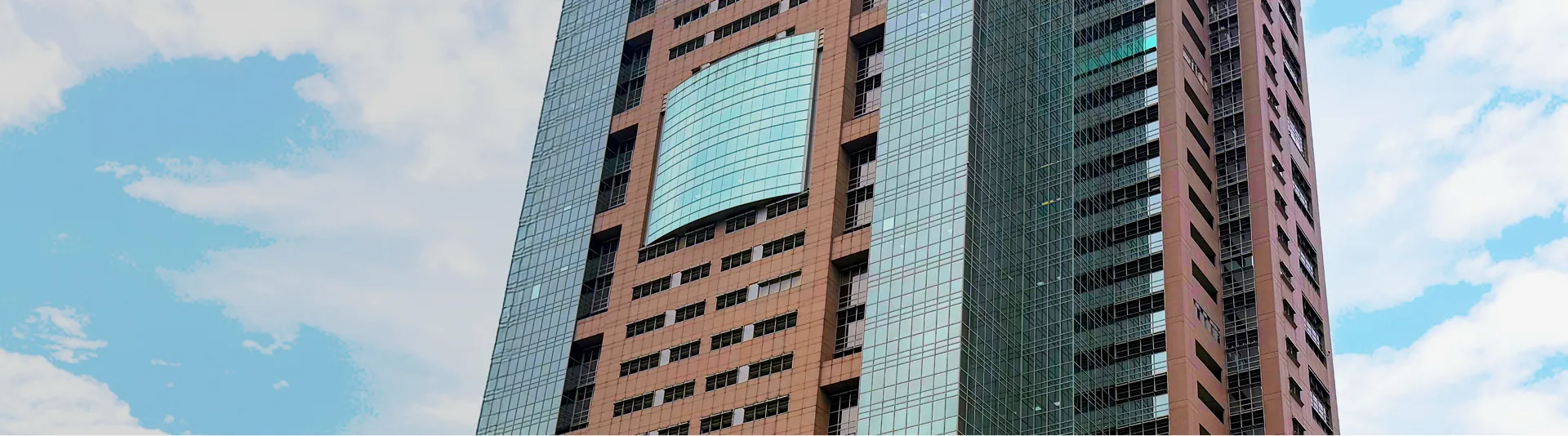 赤茶色の外壁と全面ガラス張りのパーツが組み合わさった、モダンなデザインの高層ビルの外観。