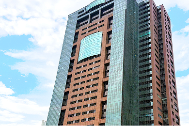 高層ビルの窓越しに広がる都市のパノラマビュー。手前には近現代的なガラス張りのビルの一部が写っている。