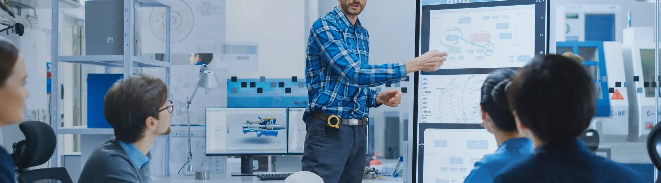 エンジニアリングオフィスでデジタルホワイトボードを使って図面を説明する男性と、それを見つめる技術者チームの風景