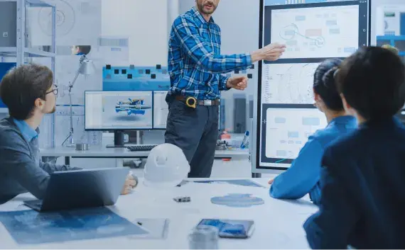 エンジニアリングオフィスでデジタルホワイトボードを使って図面を説明する男性と、それを見つめる技術者チームの風景