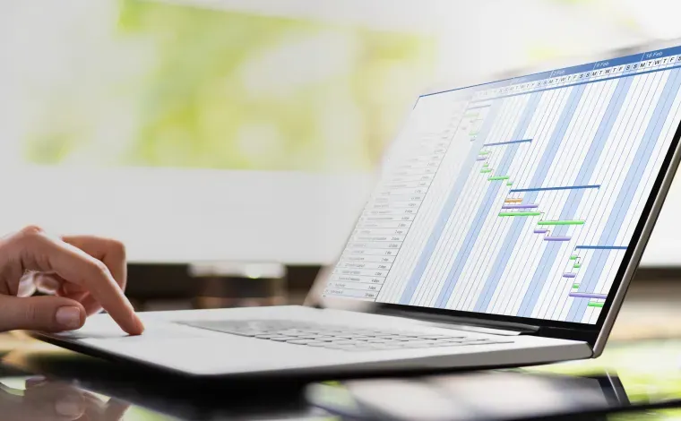 ノートパソコンの画面に表示されたガントチャートとプロジェクトを管理する手元