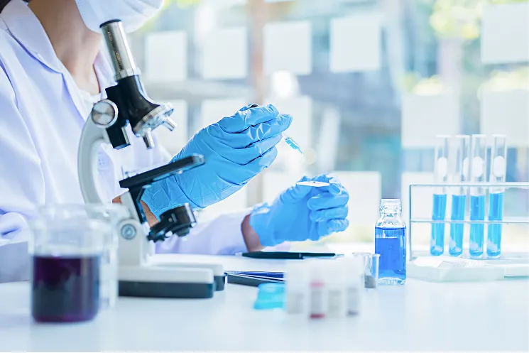 白衣を着た研究員が、研究室で試験管や顕微鏡を使って実験をしているイメージ。